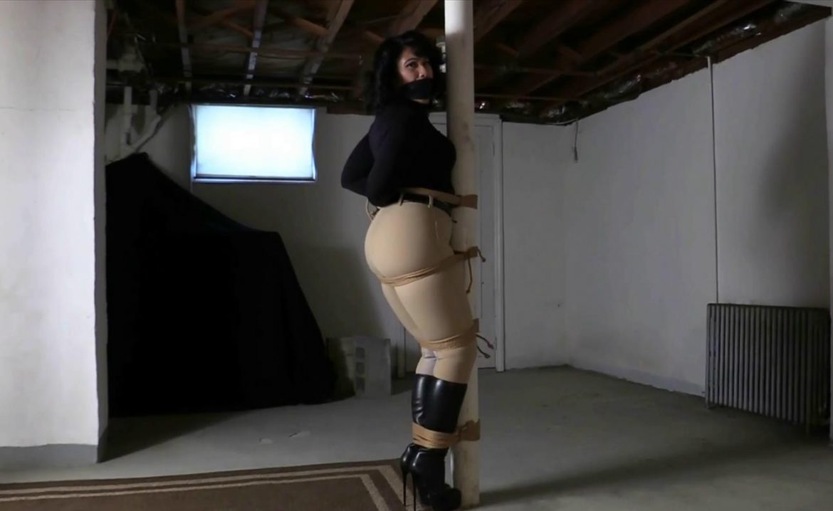 Rope bondage - Equestrian Mistress Enchantress Sahrye is tightly bound to the dungeon post with unforgiving jute rope - She is gagged with a black leather strap gag